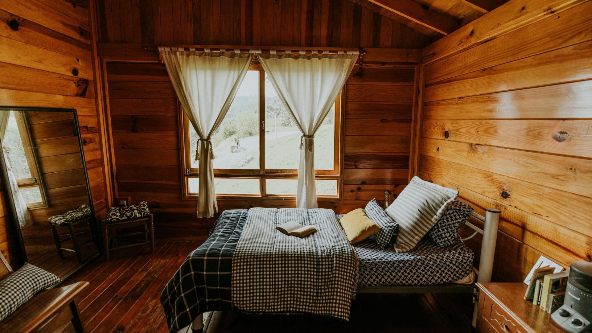 Cozy wooden cabin bedroom with checkered bedding and large window view