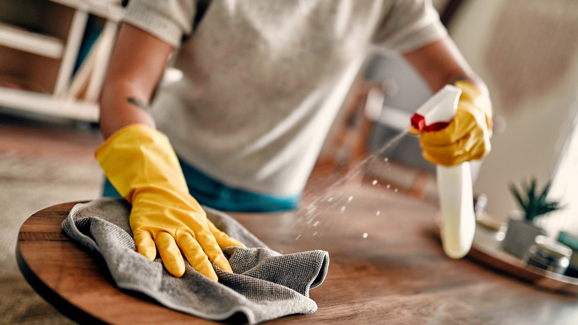 Person cleaning surface with yellow gloves and spray bottle