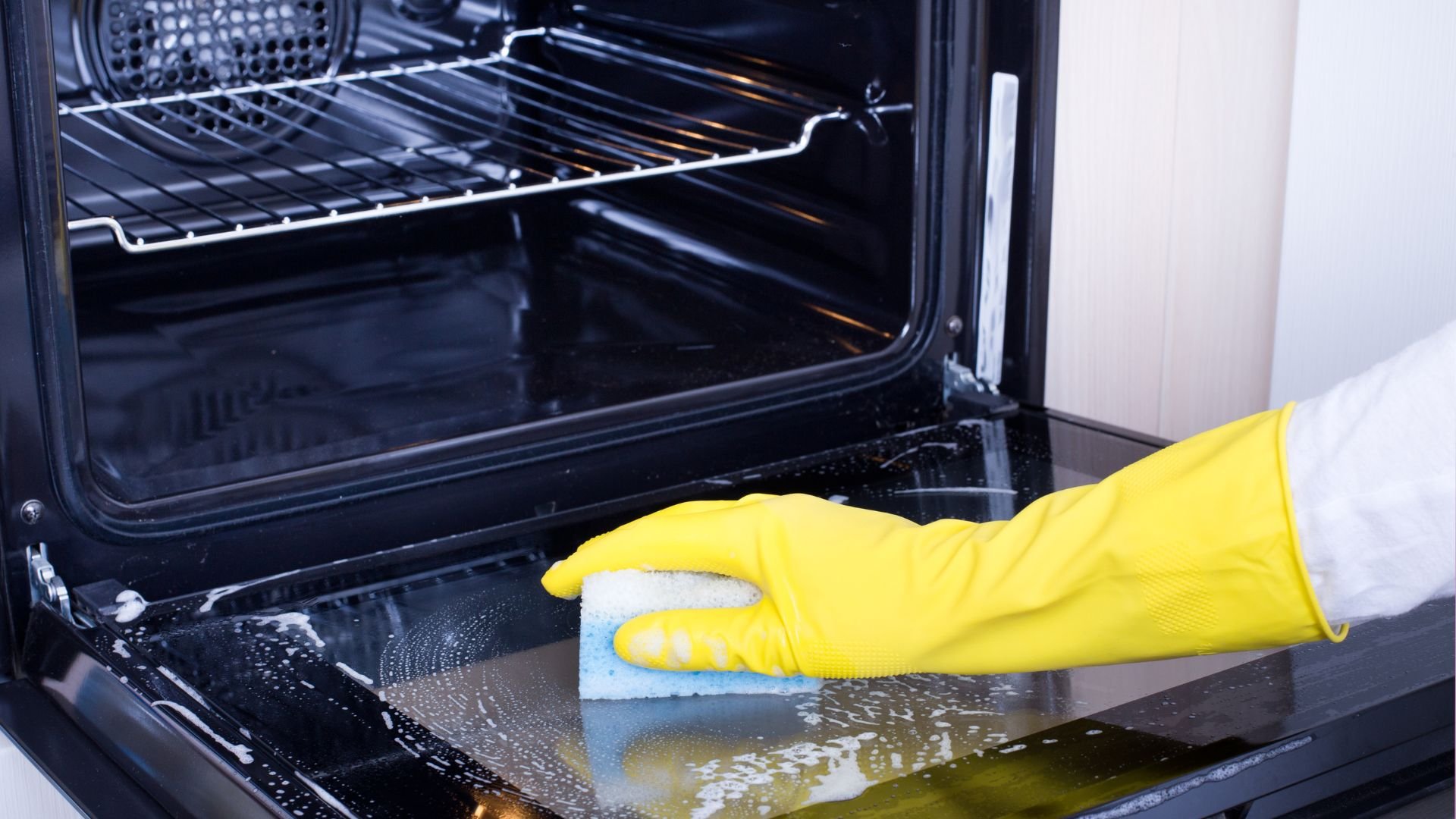 Yellow gloved hand cleaning inside of oven with sponge