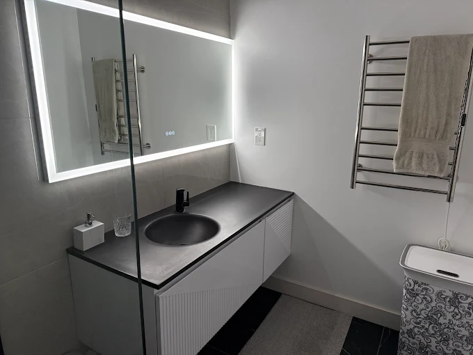 Modern minimalist bathroom with backlit mirror, black sink, and towel warmer
